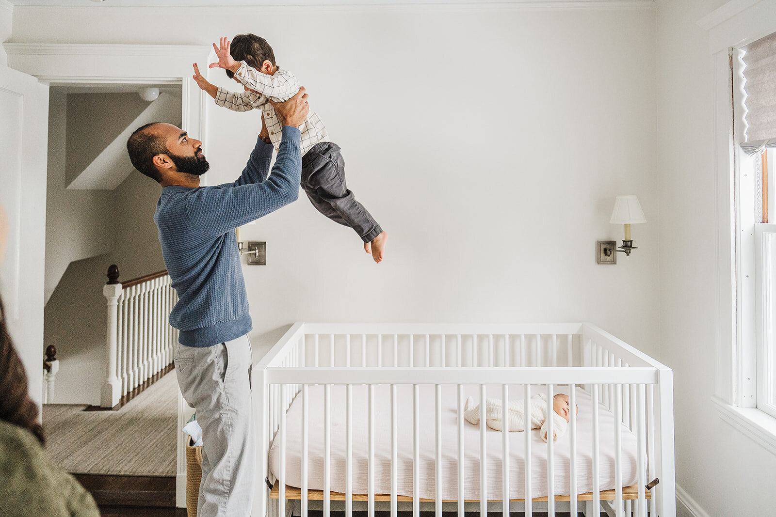 father lifts toddler son into the air in nursery