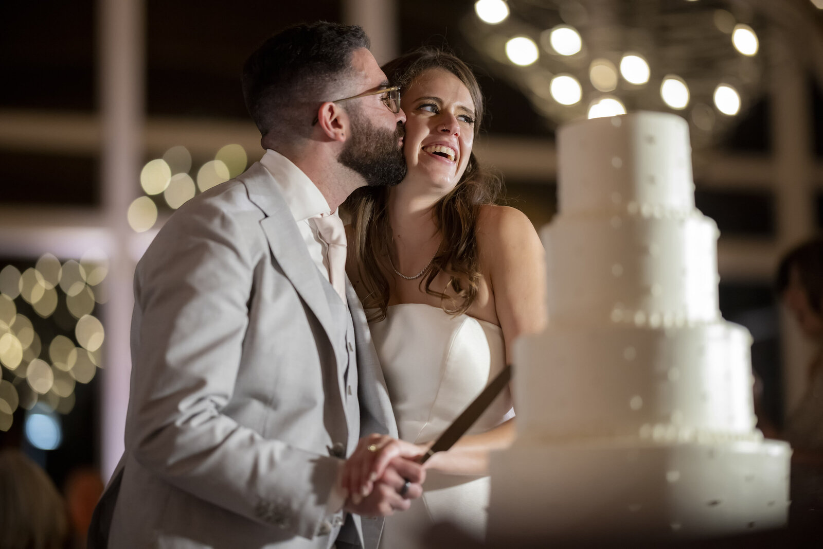 A person kissing their partner's cheek as they cut their wedding cake 