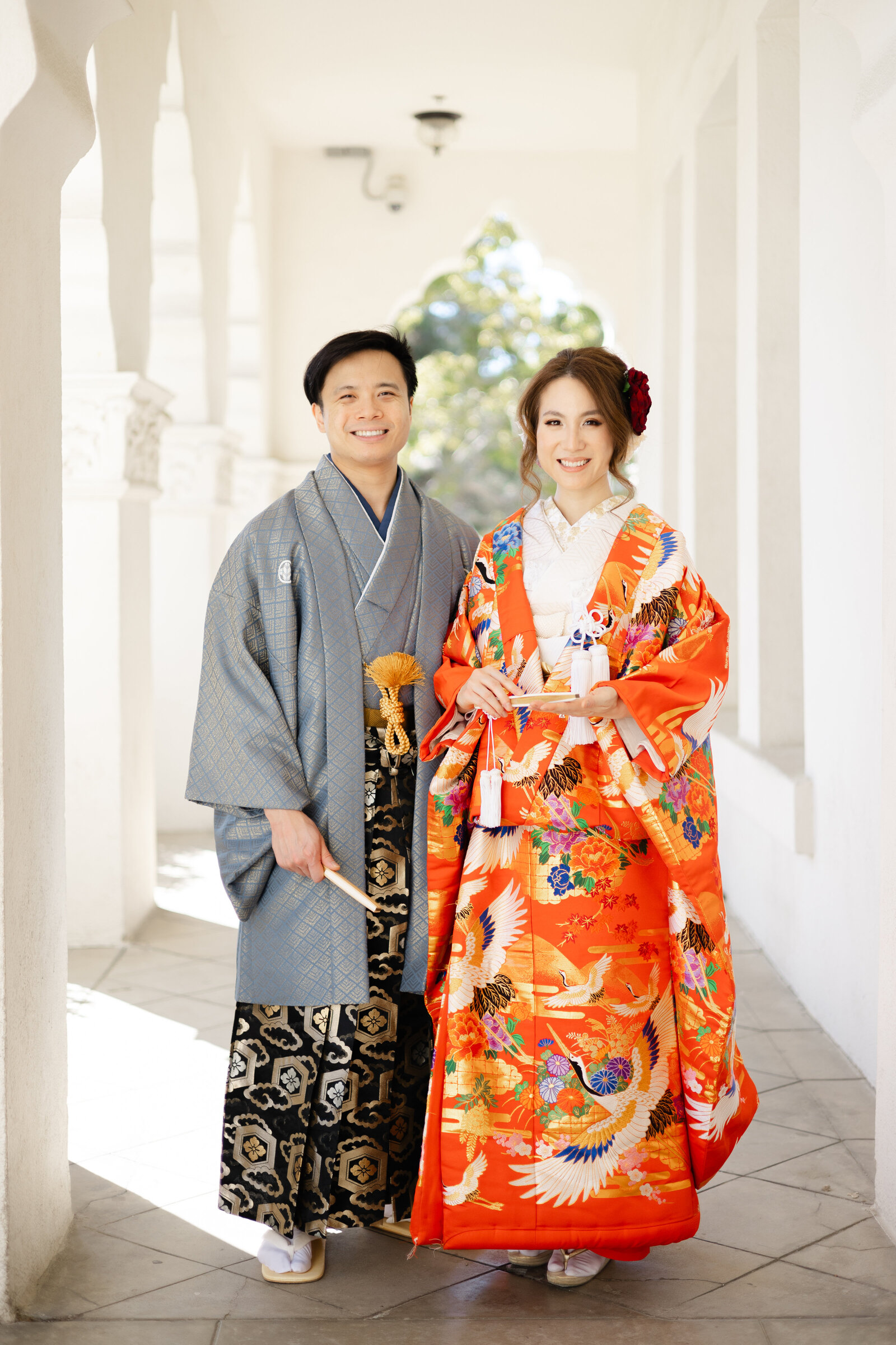 Bride in vibrant orange iro-uchikake with crane motifs and groom in blue montsuki posing at Brand Park | 着物ウェディング オレンジ色打掛 鶴柄 新郎新婦 ブランドパーク