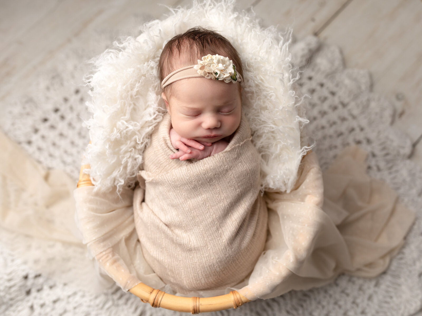 newborn baby girl wrapped in beige swaddle laying in basket for studio portraits