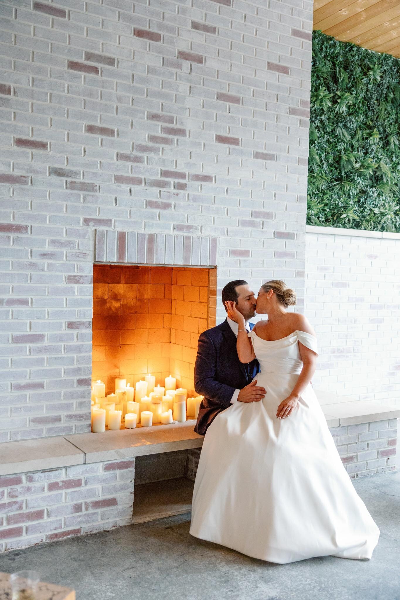 a bride and groom sit together in front of a white brick fireplace sharing an intimate moment on their wedding day at grbic events, a wedding venue in st. louis