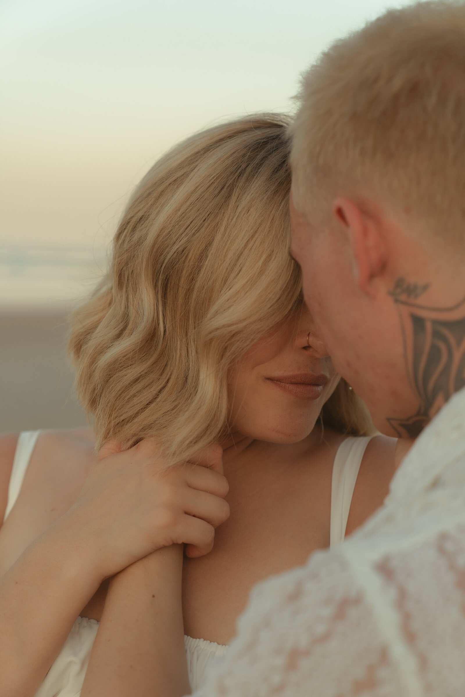 Romantic close-up of a couple holding hands and touching foreheads on the beach during golden hour.
