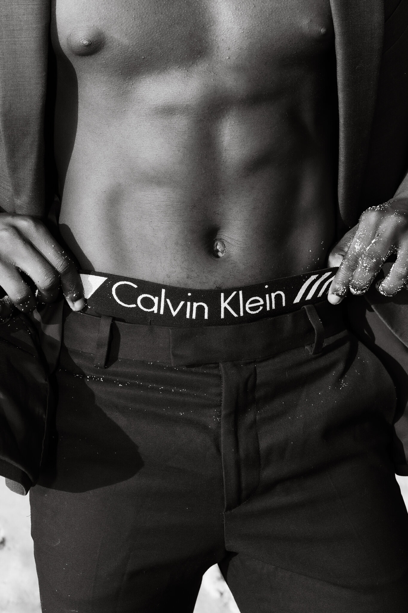 Close up of man holding up pants while showing the label of boxer brand with sand grains on his fingers and trousers