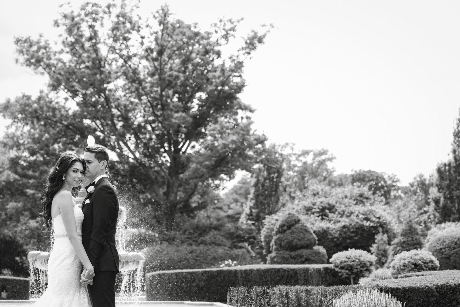 Black and white photo of bride and groom by the fountain of Glen Cove Mansion