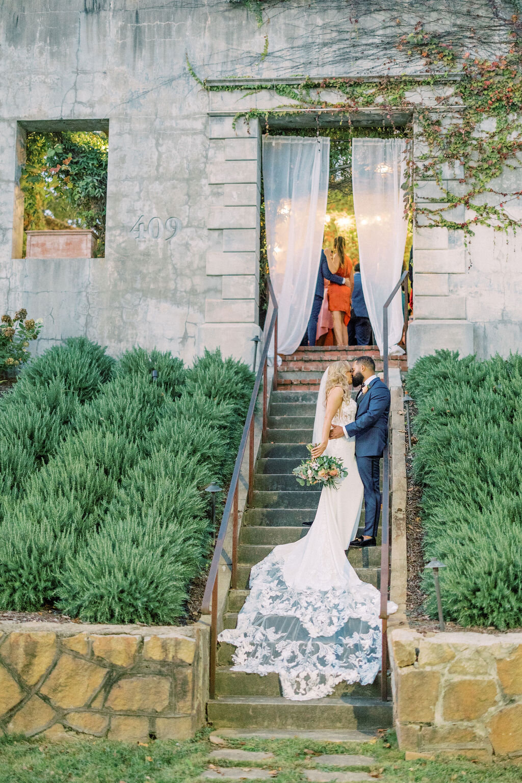 Groom kisses bride with long white dress on brick steps outside Summerour Studio in Atlanta