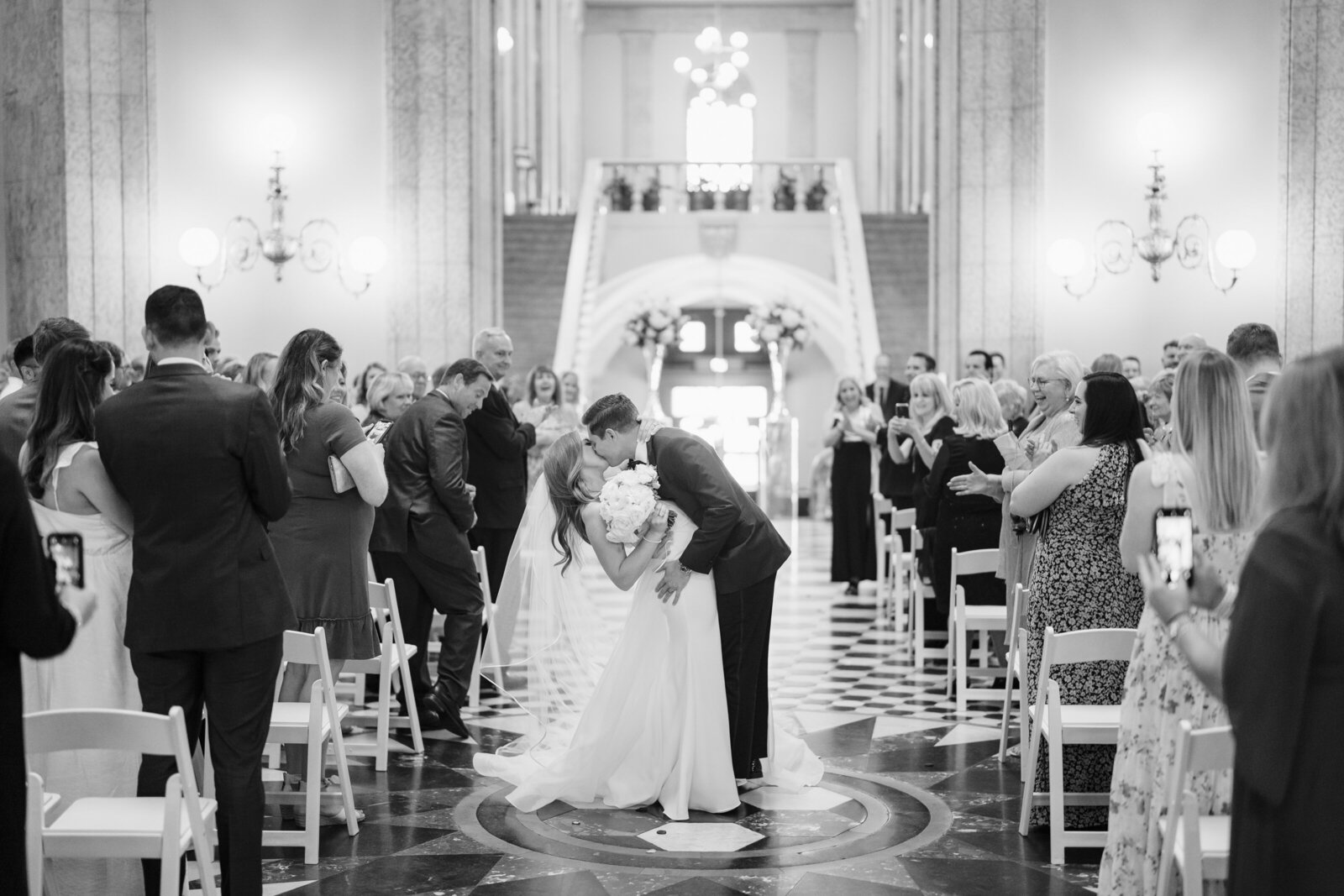 Groom dips his wife for a kiss inside the Rotunda of the Ohio Statehouse as their guests look on and celebrate