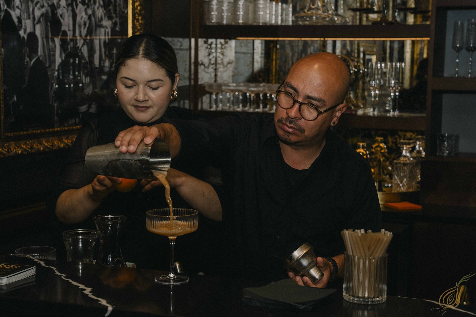 A man and woman are skillfully preparing drinks together at an after party event at the bar, showcasing their mixology talents.