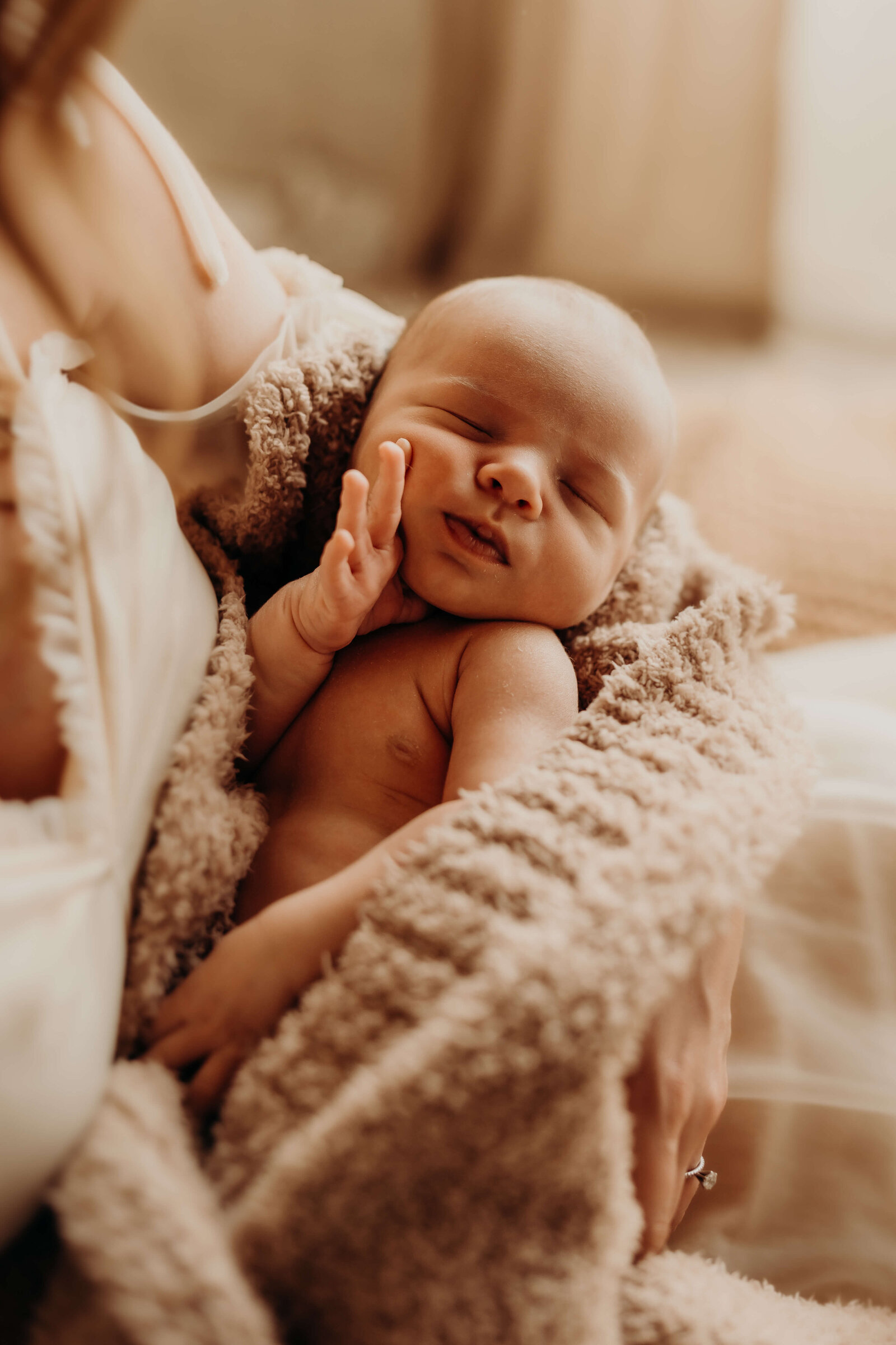 newborn baby boy holds face cuddled in fluffy blanket