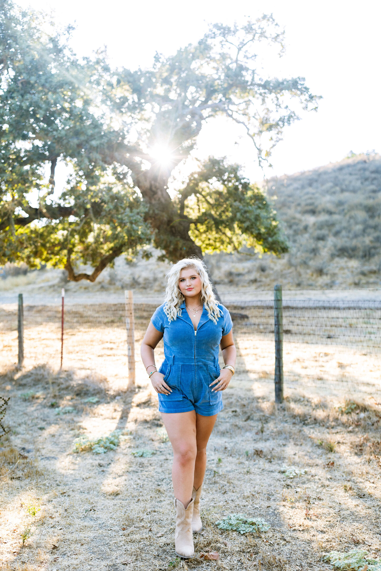 blonde girl wearing blue jean romper and cowboy boots posing on a ranch