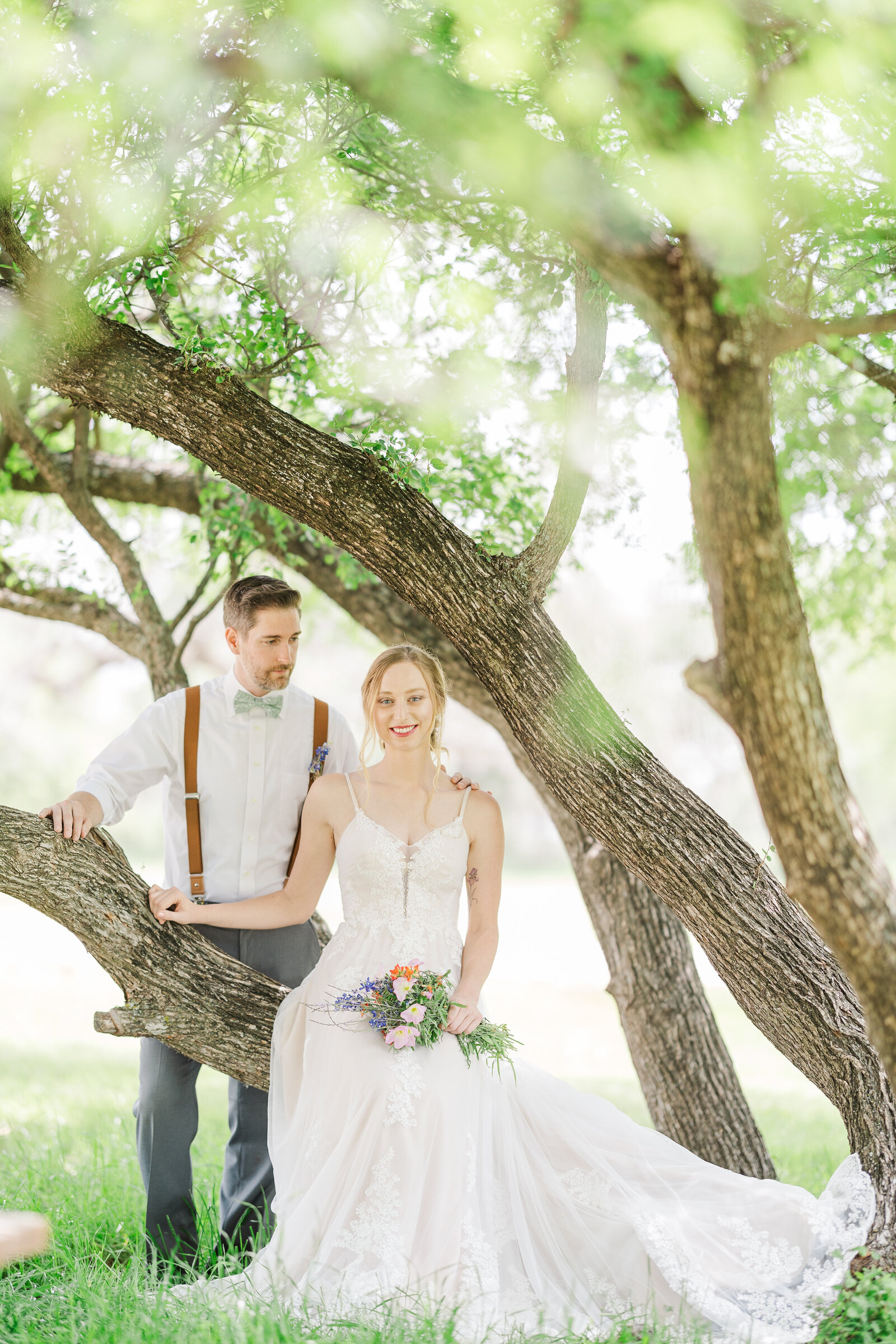 Bride-sitting-on-tree-branch-groom-standing-behind