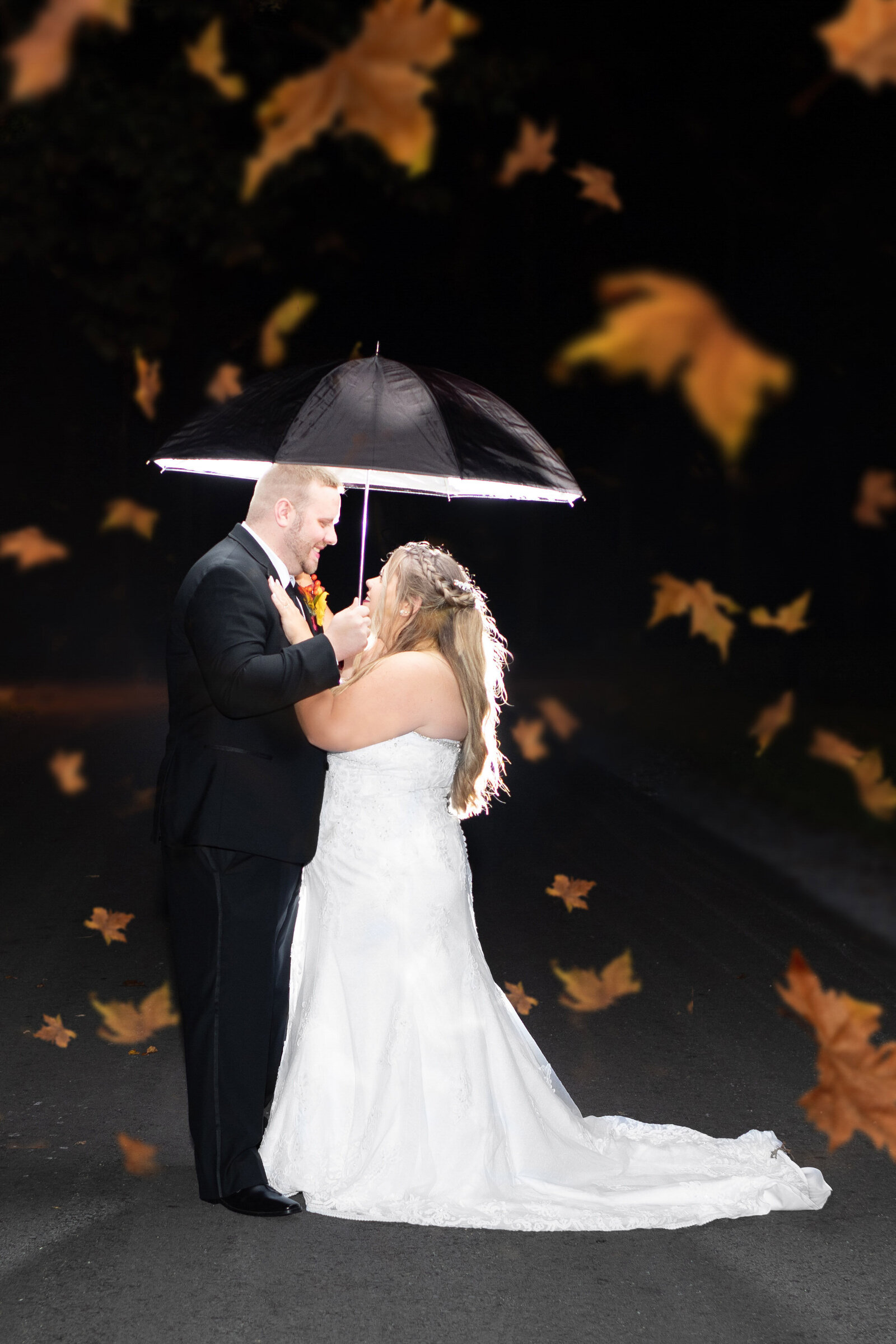 The bride and groom share an intimate moment under a glowing umbrella with falling leaf effects at night, captured during a Blue Knob, PA wedding, blending romance with seasonal charm.