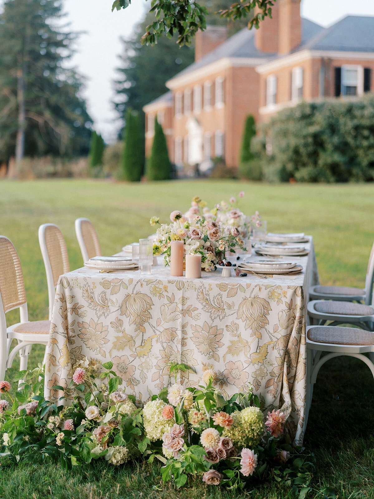 Long table overlooking Harford Hills mansion with ground arrangement at the end of the table including green hydrangea, mauve garden roses, peach and orange dahlias, blush lisianthus and organic greenery.