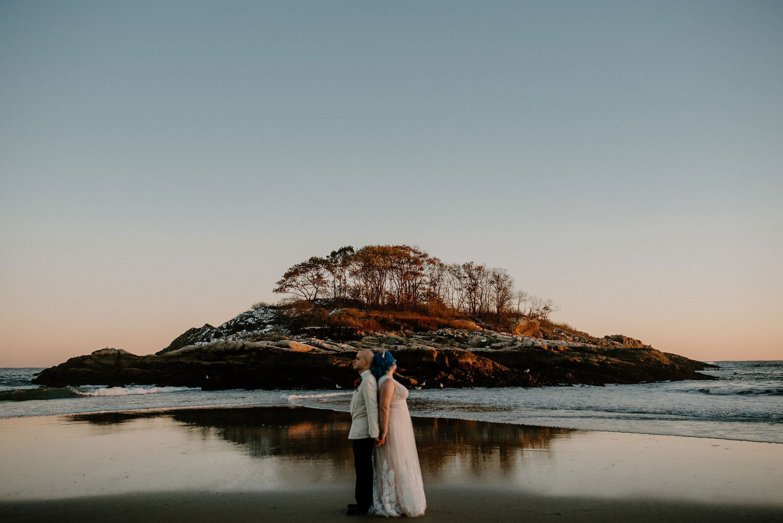 couple standing back to back at the water’s edge near island at sunset along Massachusetts coast