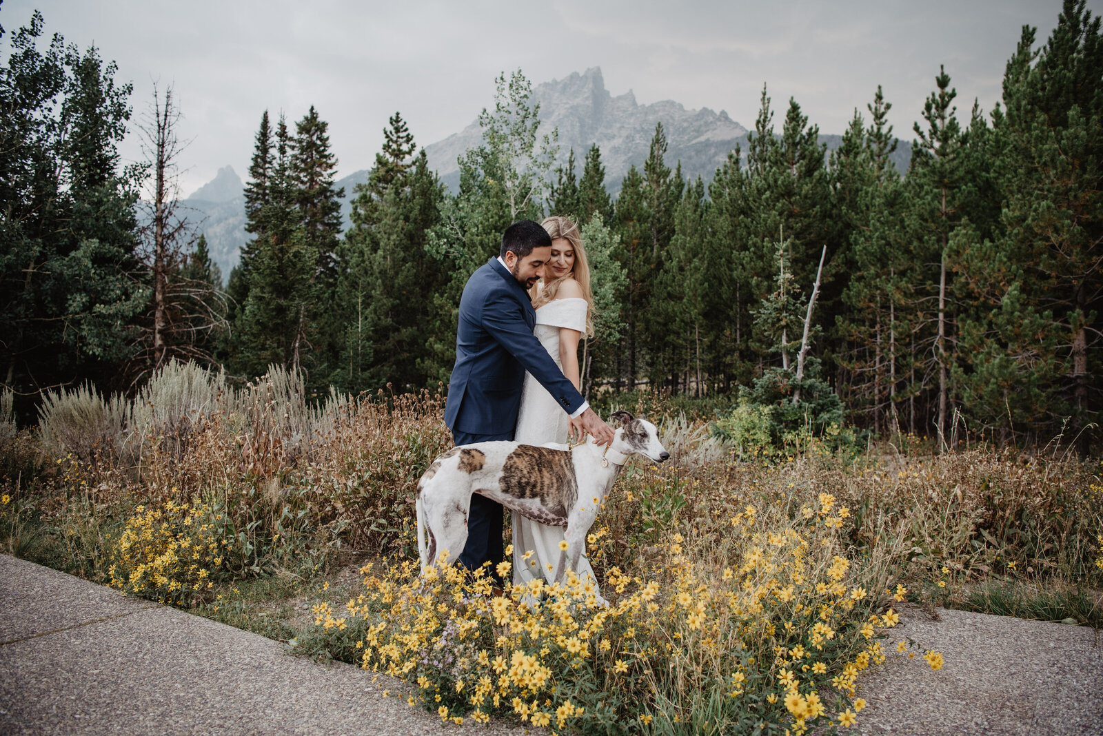 bride and groom stand among yellow wildflowers with their dog for their grand teton wedding pictures captured by jackson hole photographers in the fall