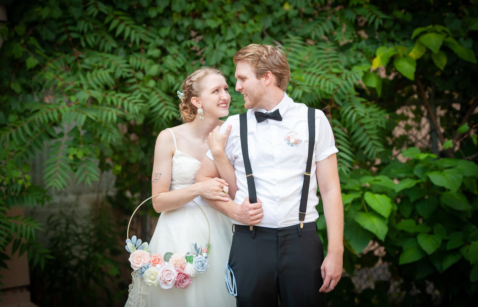 bride holds groom in suspenders smile at each other