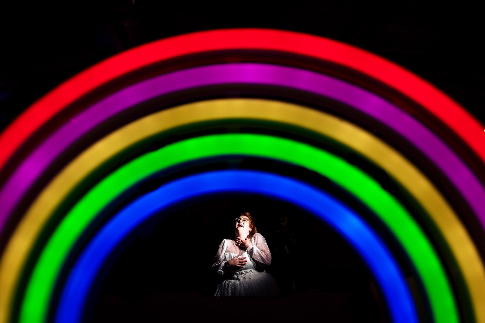 creative wedding photography of a bride laughing on the dance floor with a neon rainbow sign in the foreground