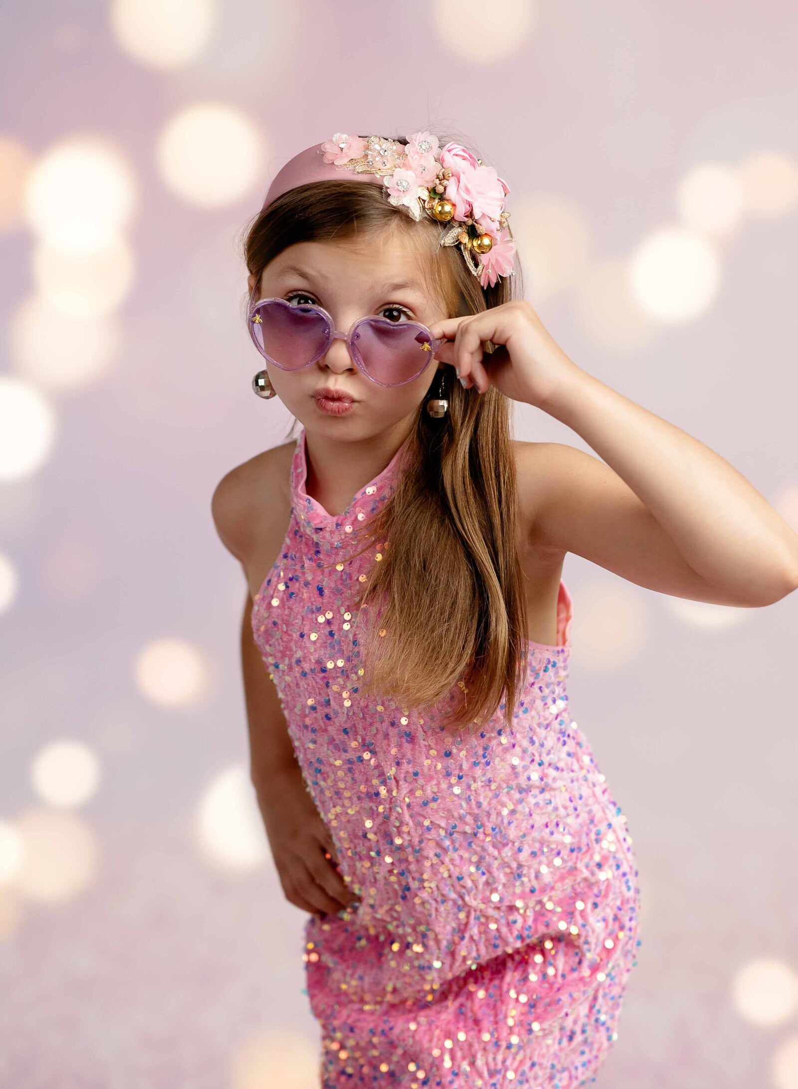 8 year old girl in pink sparkles dress with heart glasses on and blowing a kiss. Photographed at Atlanta Birthday photo studio.