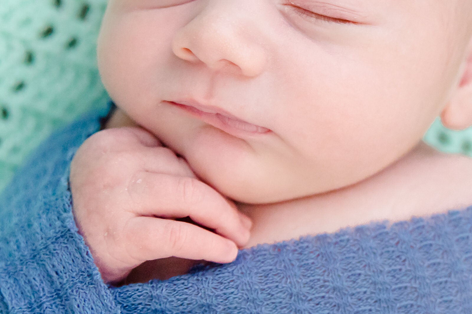Close up photo of sleeping newborn baby placing his hand by his face while staddled