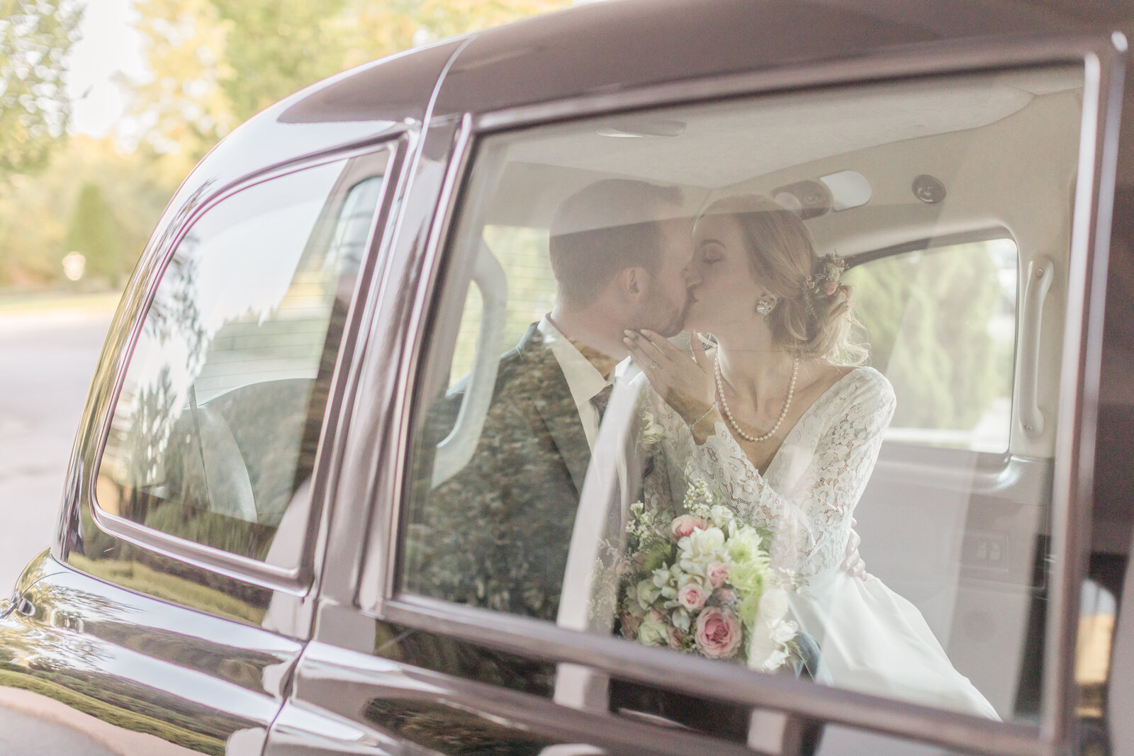 Bride and groom in get away car kissing at their wedding
