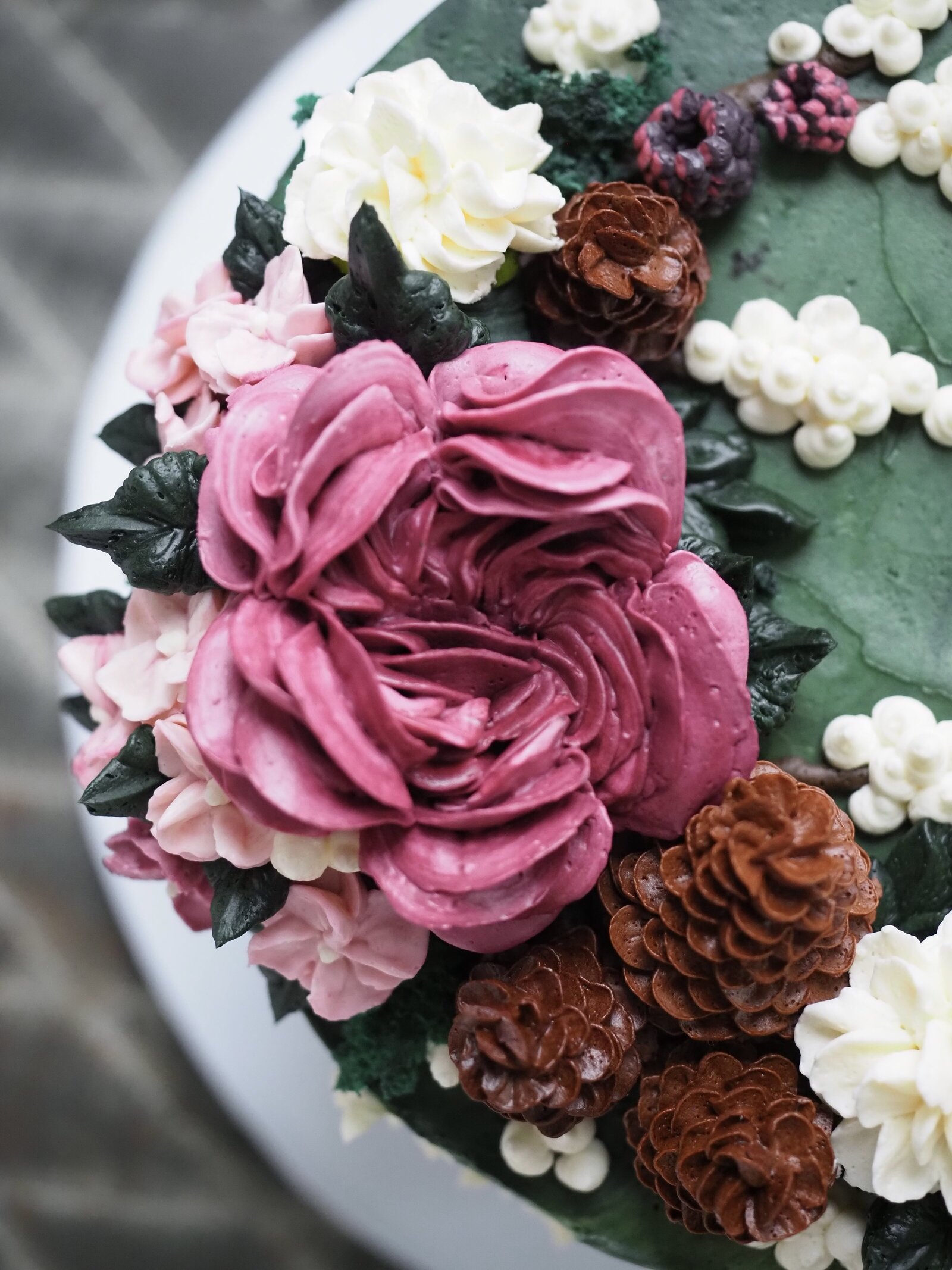 Close up of buttercream flowers and pine cones on a cake