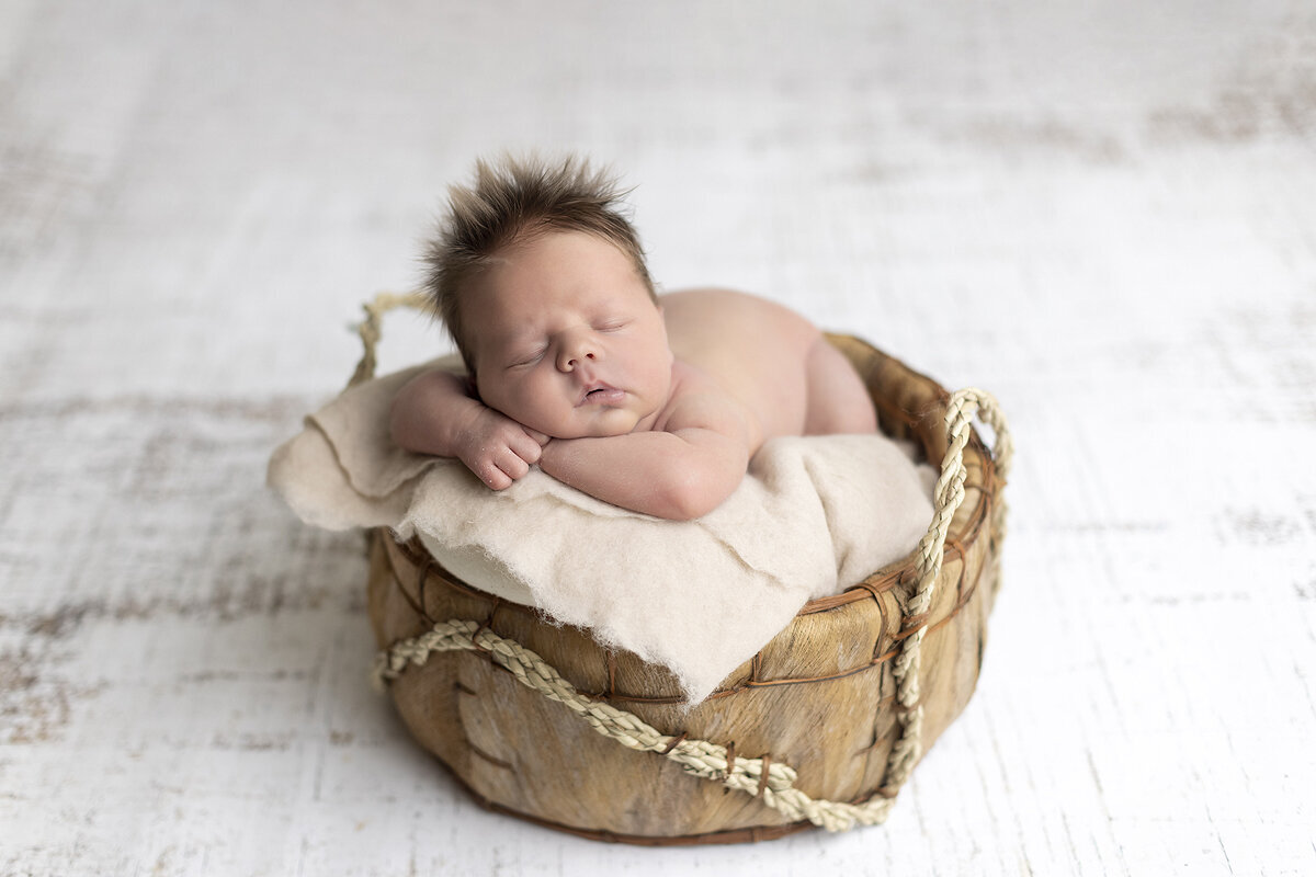 Newborn boy posed in basket.