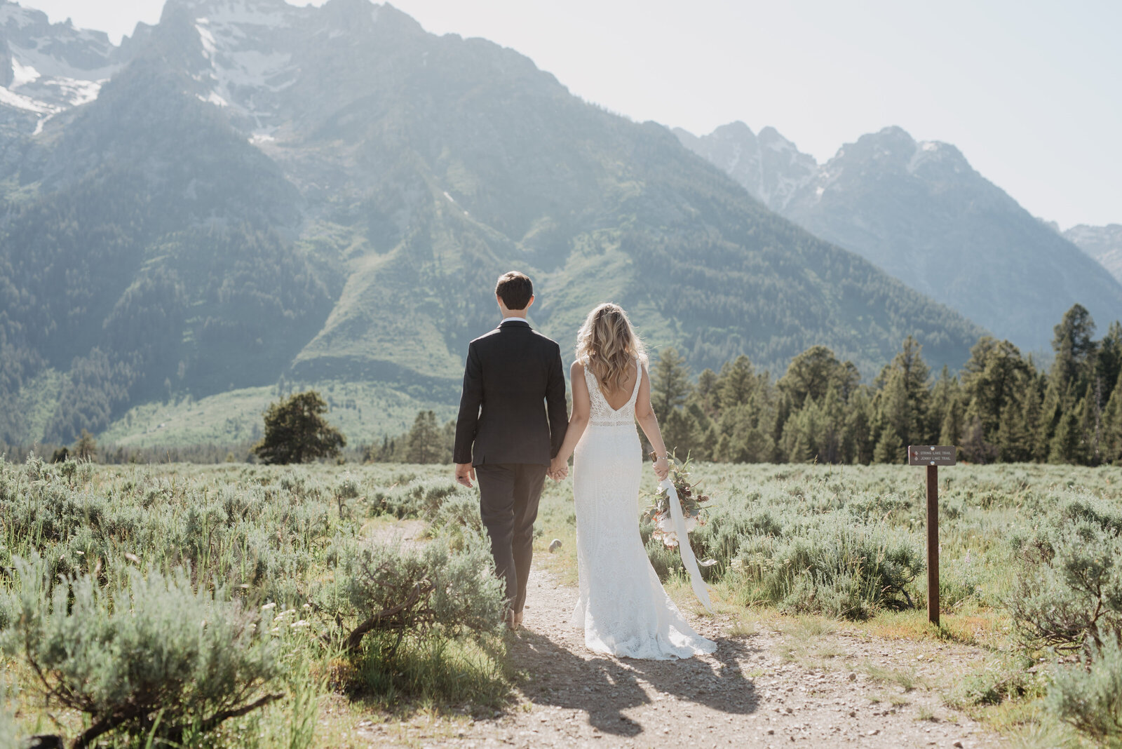 jackson hole wedding with bride and groom holding hands and walking on a dirt path in the grand tetons