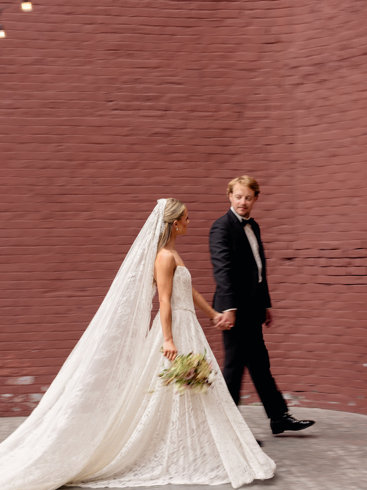 Aubri and Cody walking hand in hand past a red brick wall