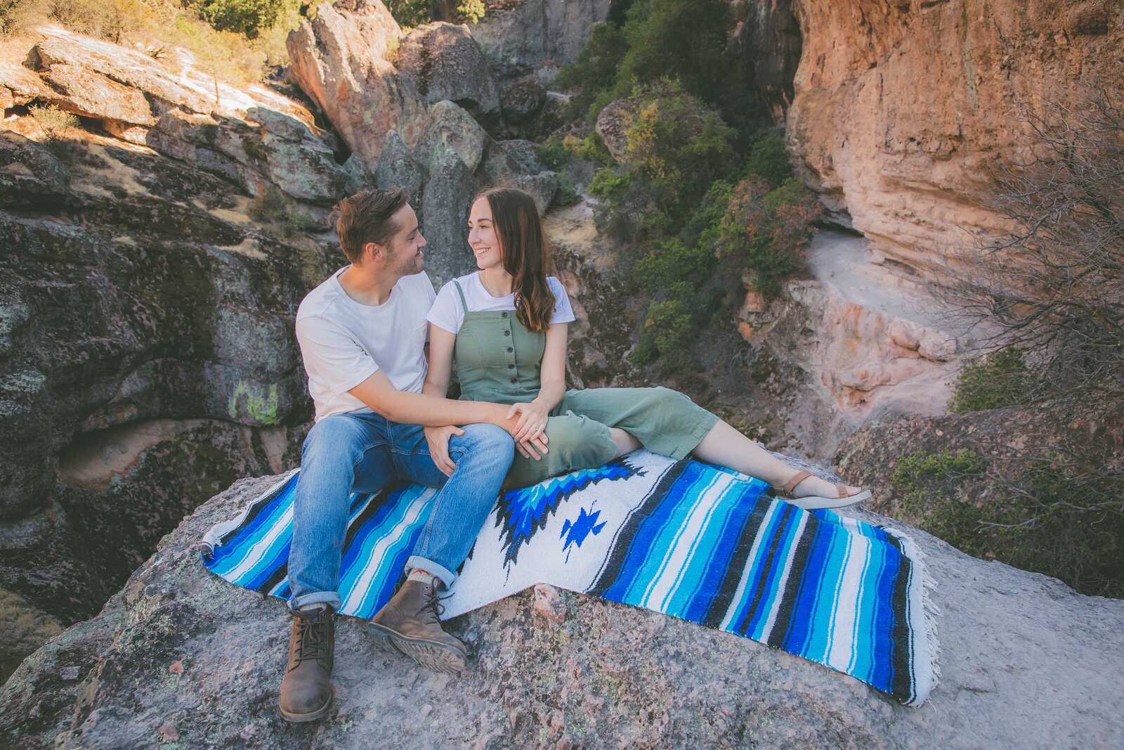 A couple sits down on a blue blanket at Pinnacles National Park during their adventure session.