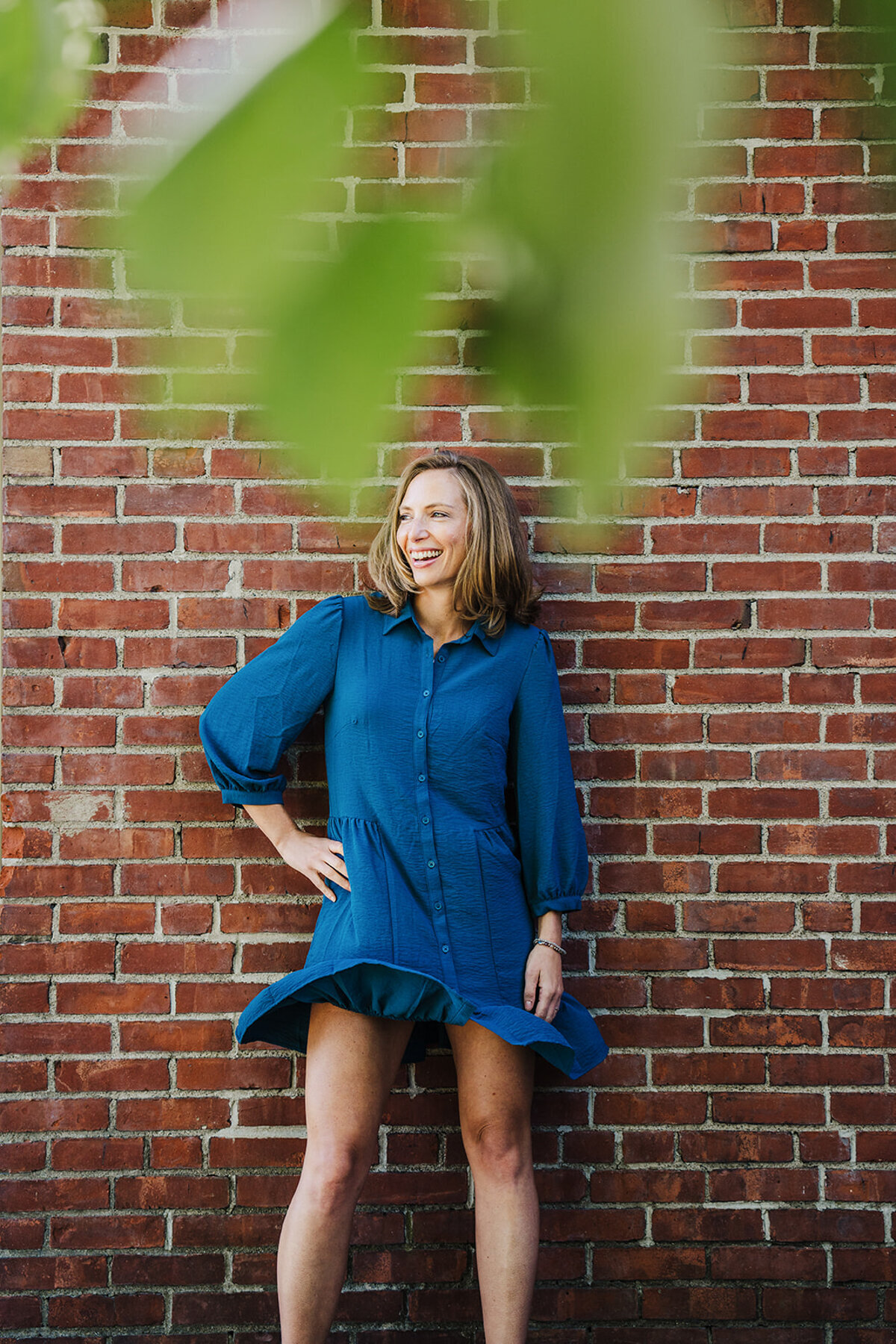 woman in blue dress laughs against a brick wall