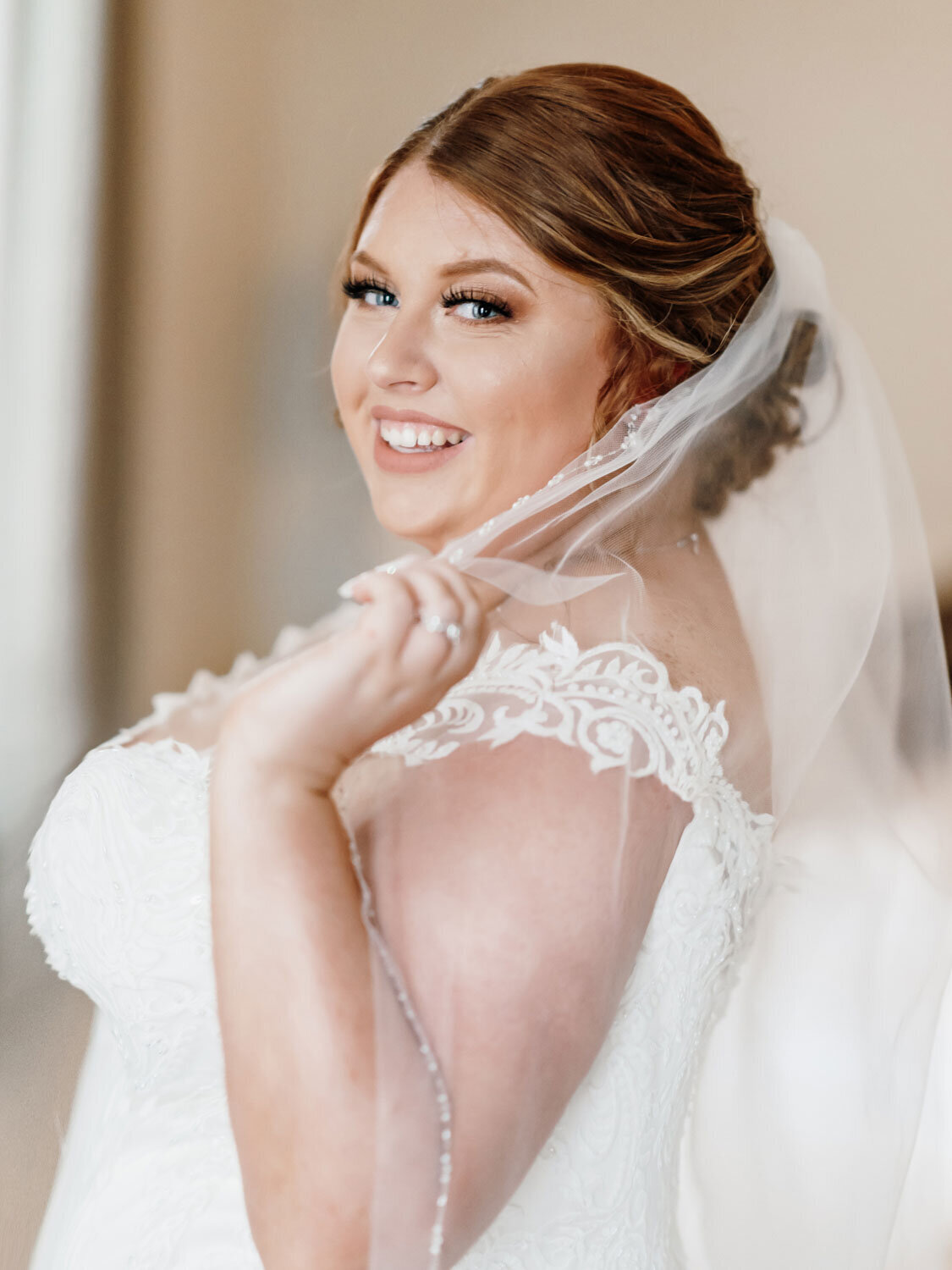 A bride smiling over her shoulder, showcasing her intricate veil and gown