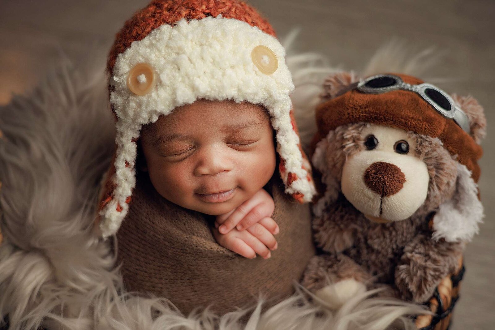 A charming newborn boy with a hat, holding a teddy bear, beautifully captured by Bia Schaefer in a home setting.