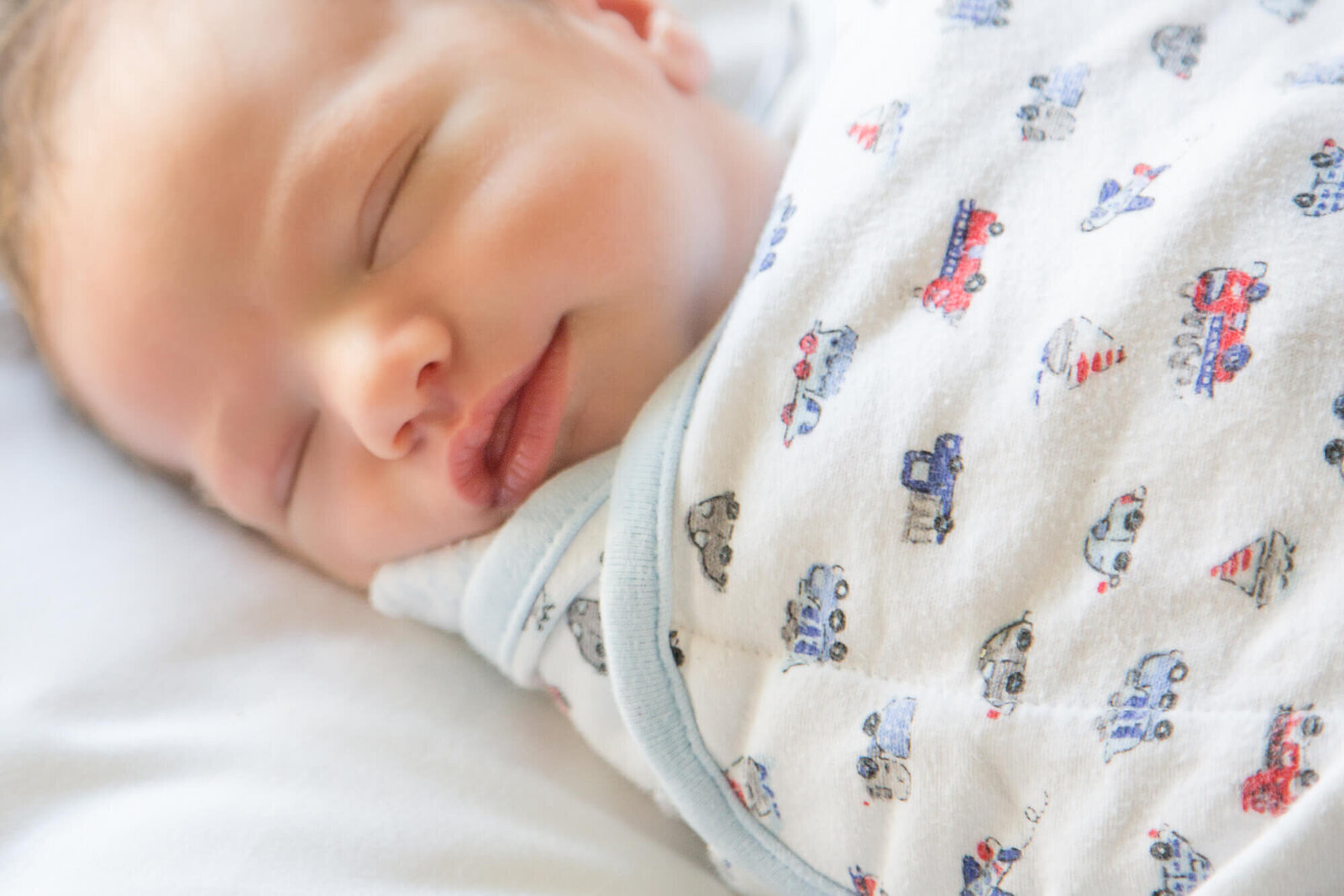 sweet newborn baby boy wrapped in a swaddle with cars on it