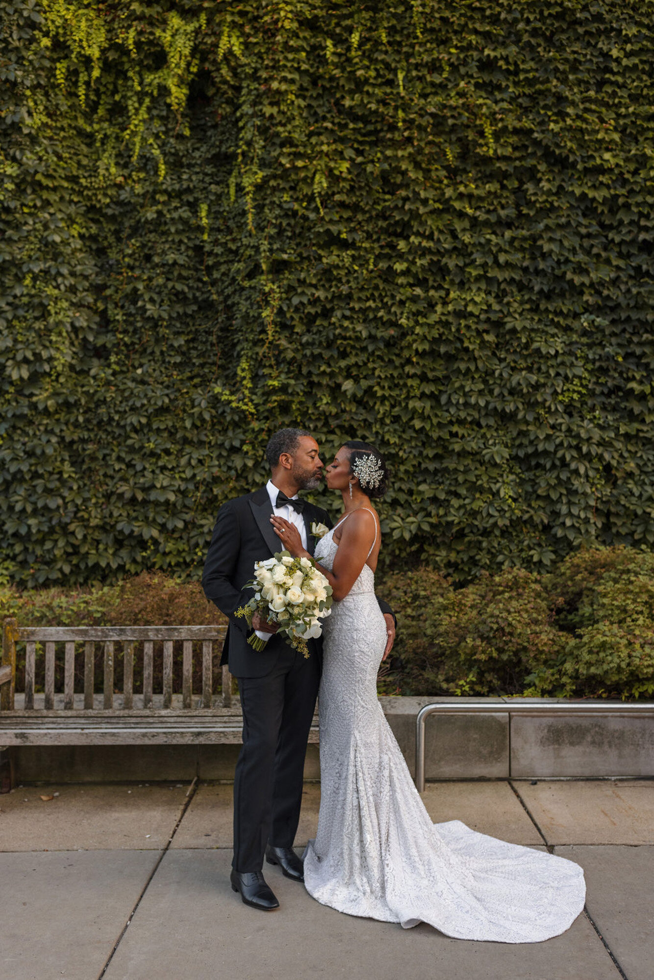 bride and groom kissing in front of ivy wall