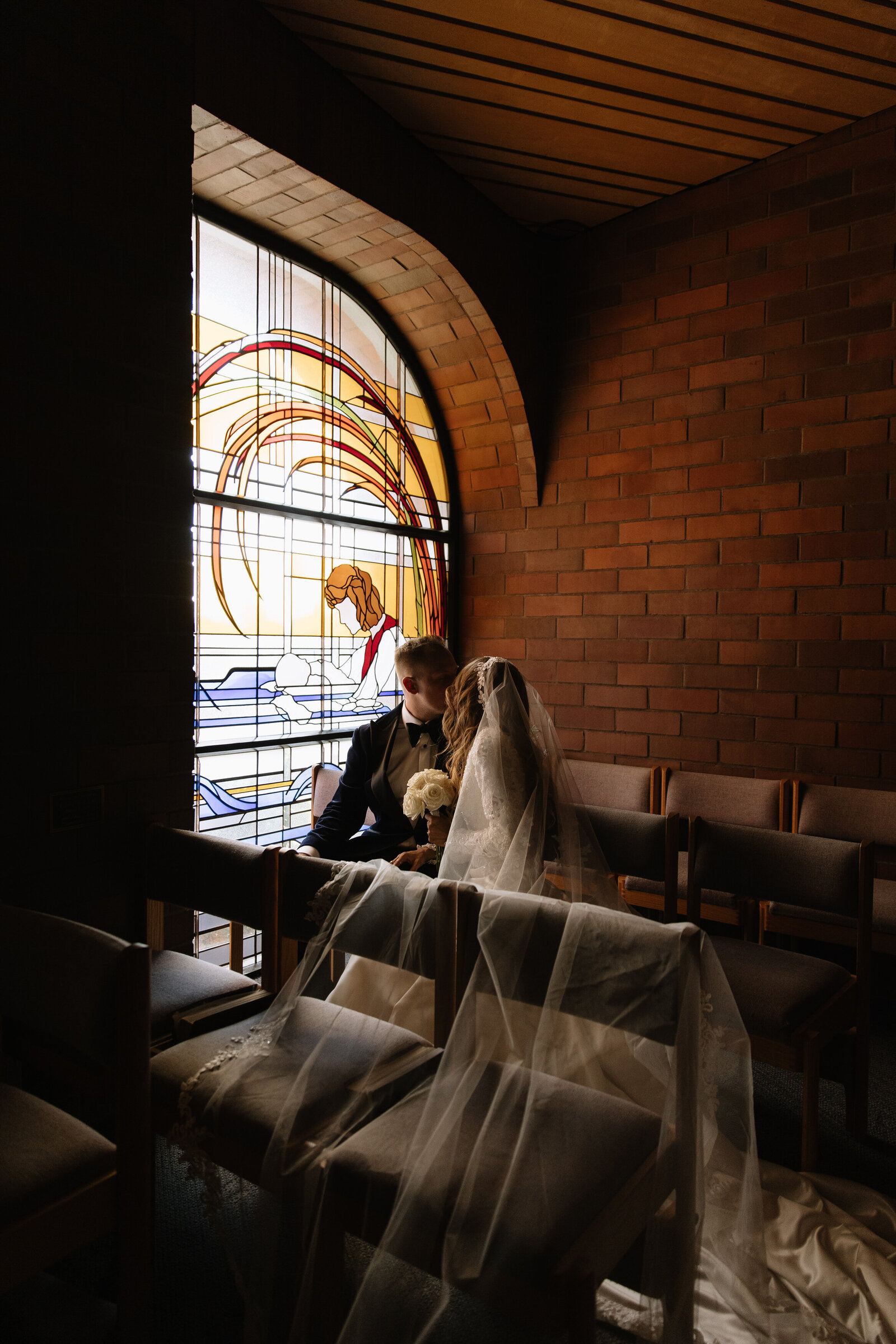 Couple sitting in Boise church pews for intimate portraits in front of stained glass windows
