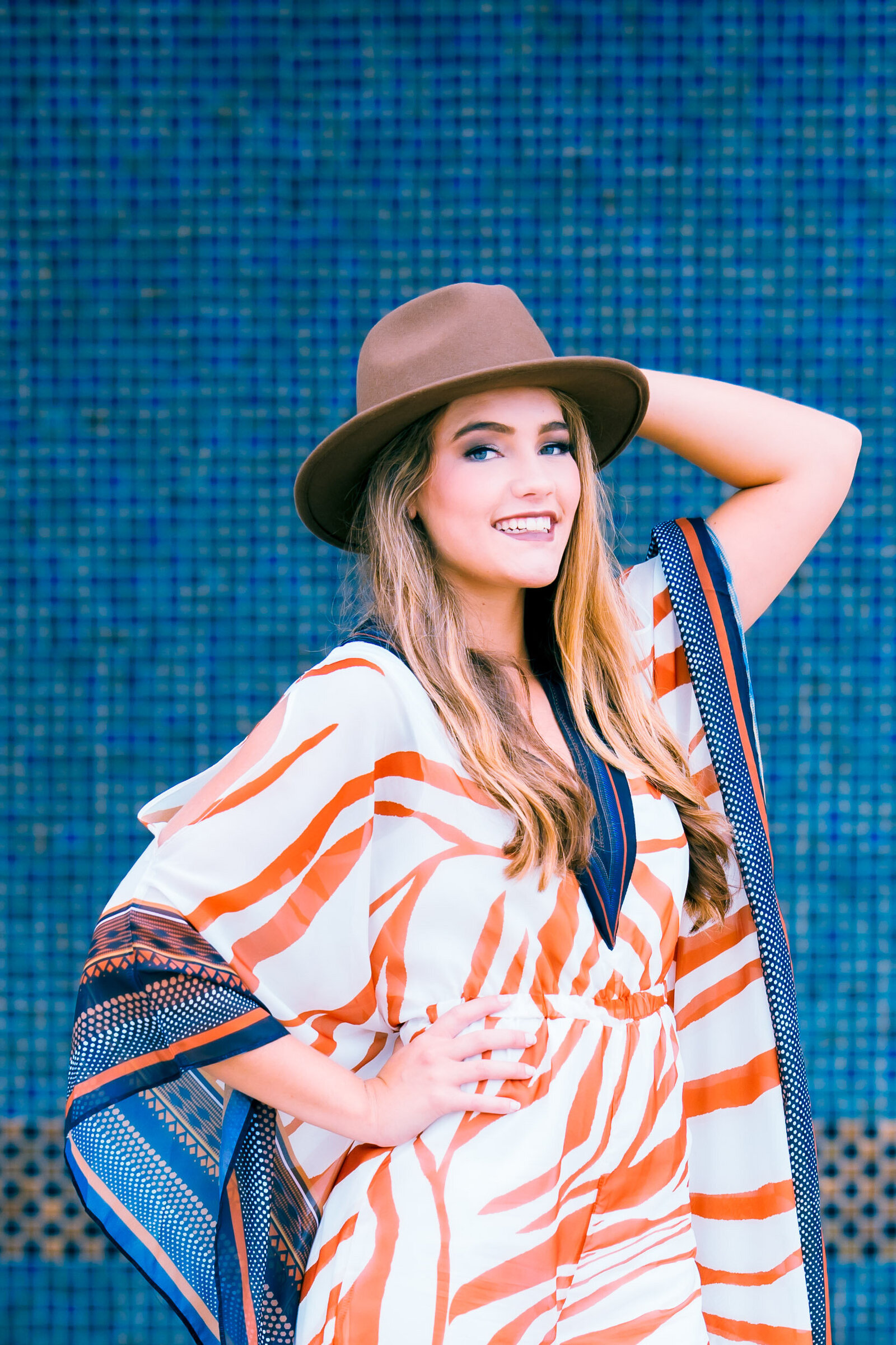 senior girl with cowboy hat posing near a teal wall in Kansas City for senior pictures