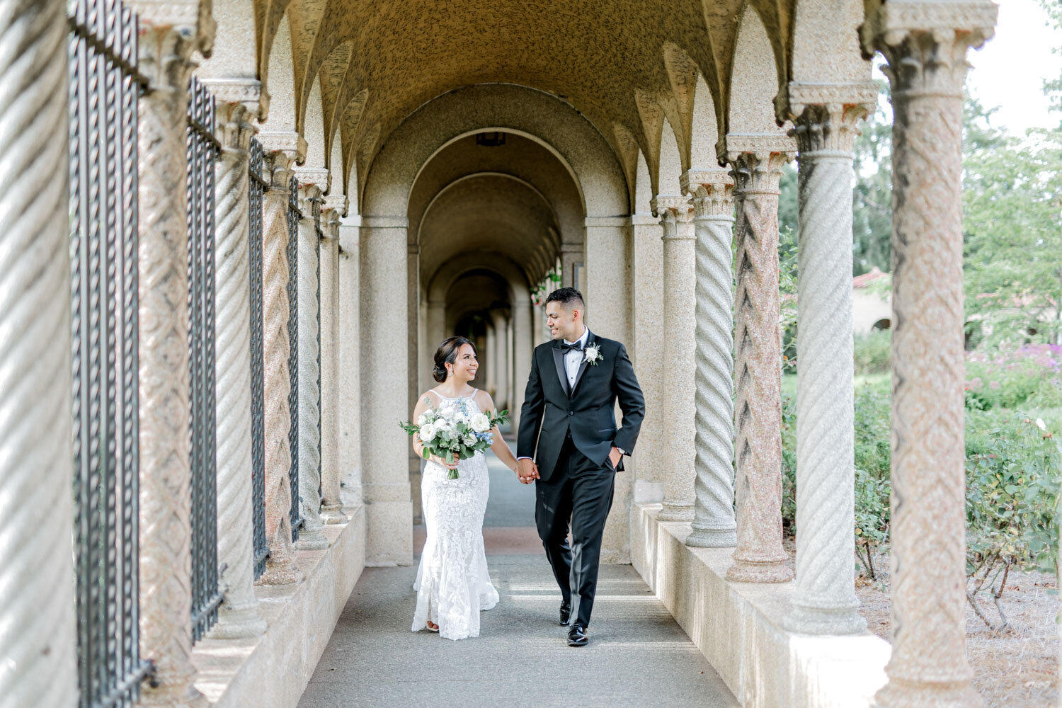 Bride and groom walking hand in hand under arched stone hallway