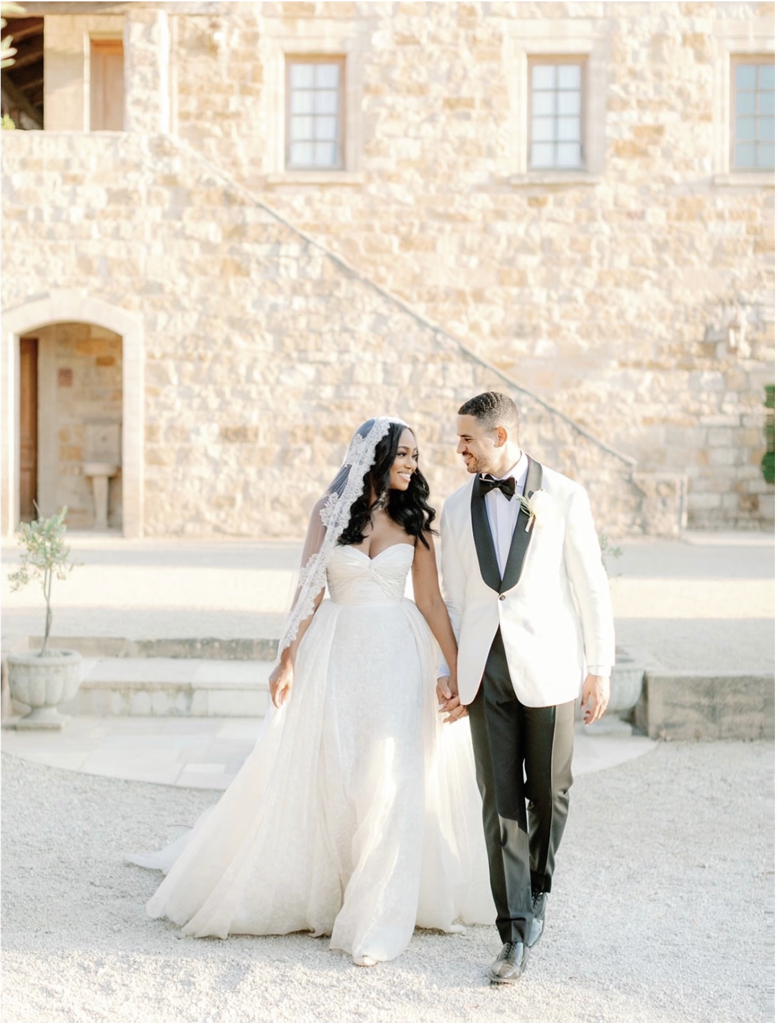 bride and groom walking outside and holding hands in front of an old stone building
