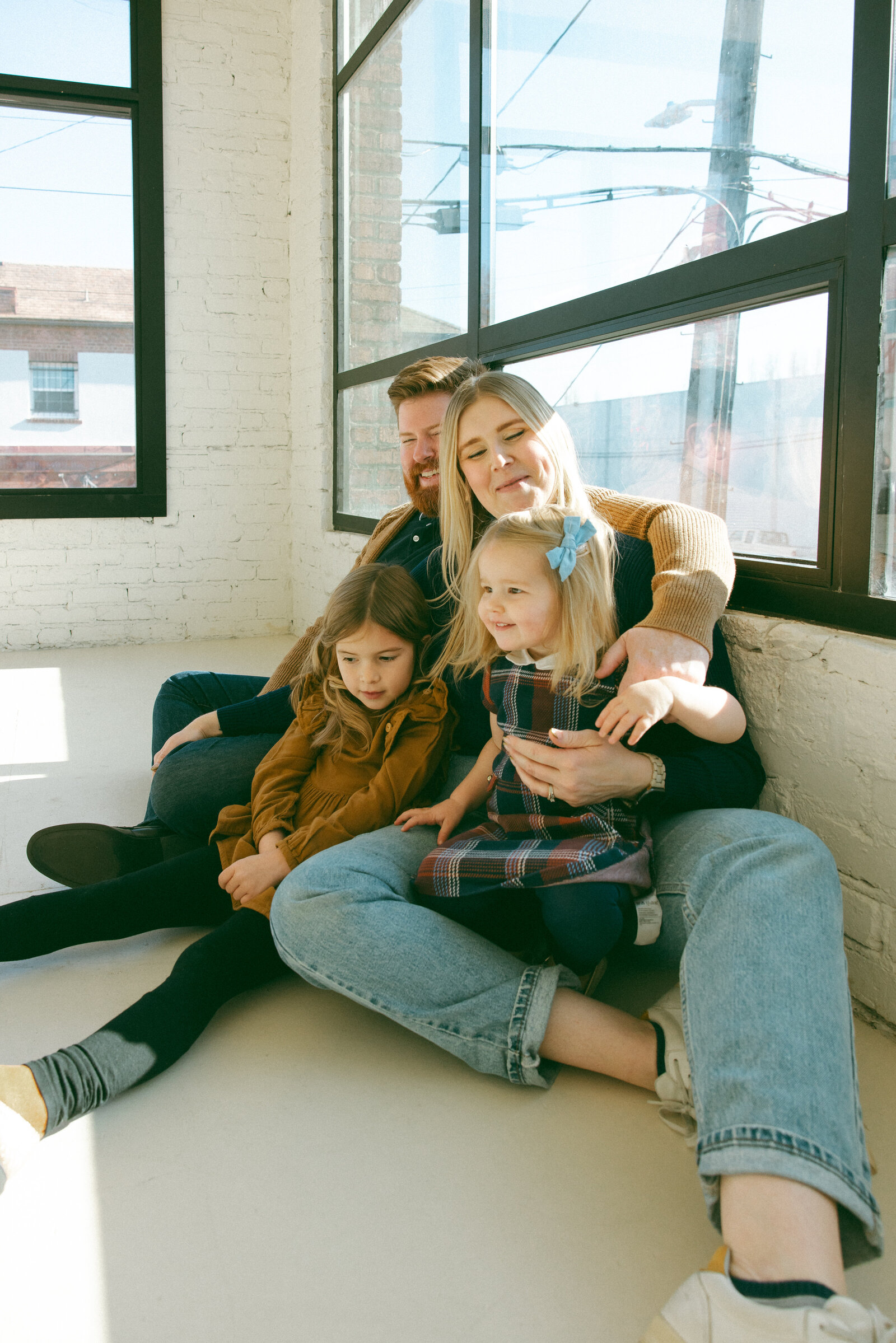 family of four sitting on the floor of a studio with large windows all around