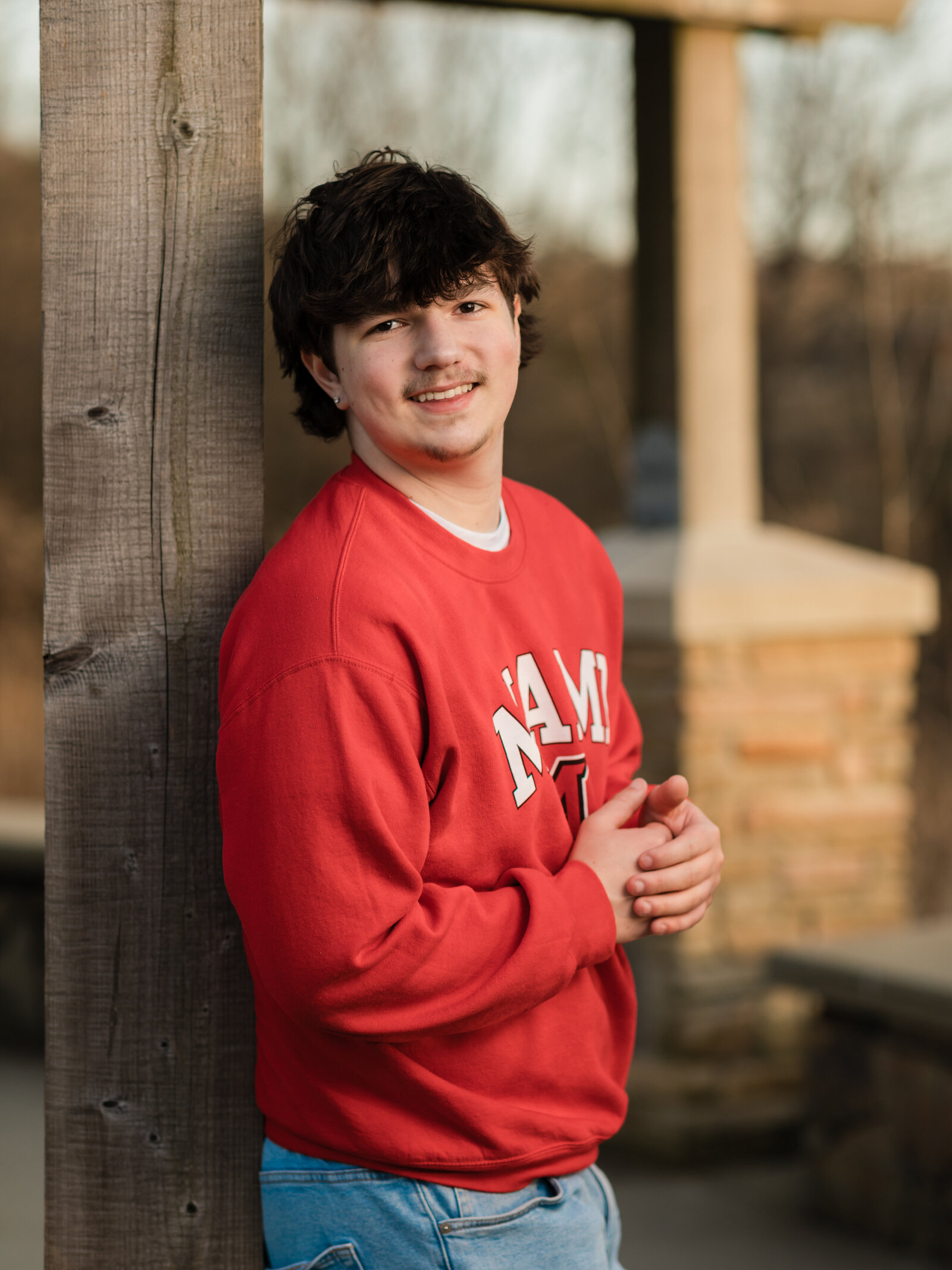 senior boy in red Miami state shirt posed for senior portraits at park Cleveland senior photographer