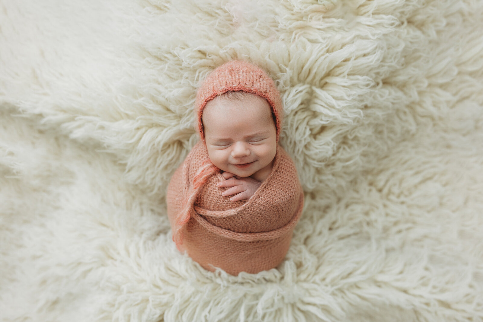 Baby girl swaddled in a soft coral bonnet and matching swaddle smiling