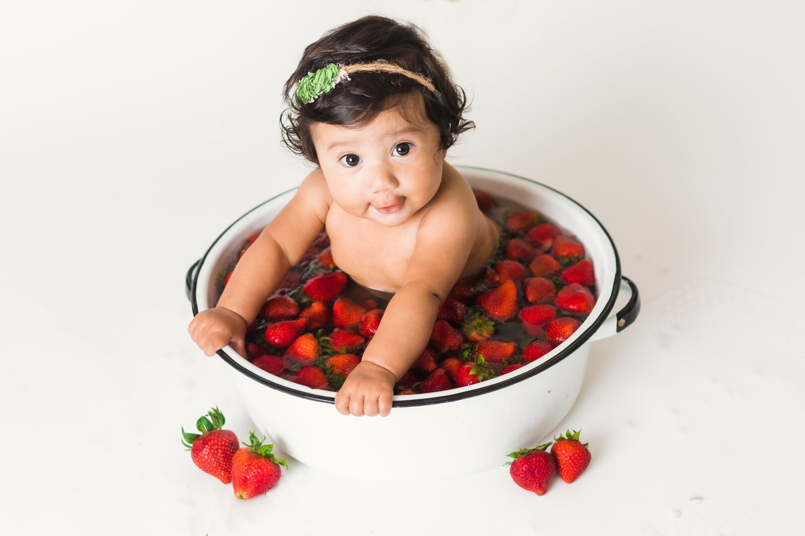 Milestone Photographer, a baby sits in a ceramic pot with floating strawberries