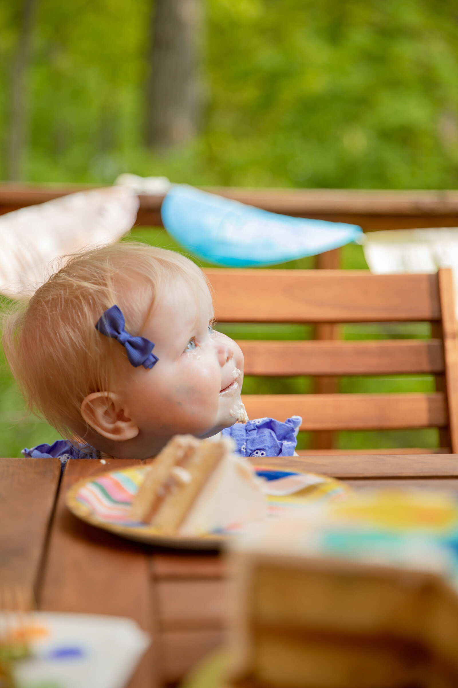one year old girl looks up to the right of camera with frosting on face and cake in foreground during sweet heather anne styled session