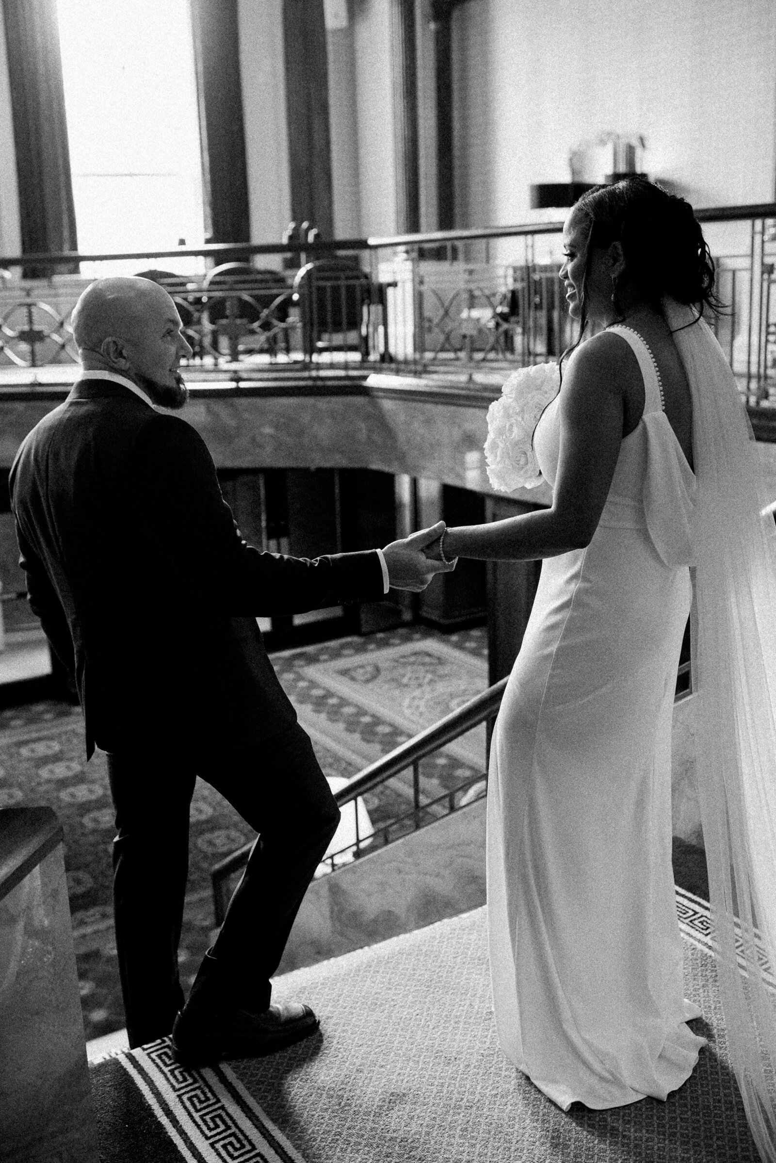 bride and groom hold hands walking down stairs from behind