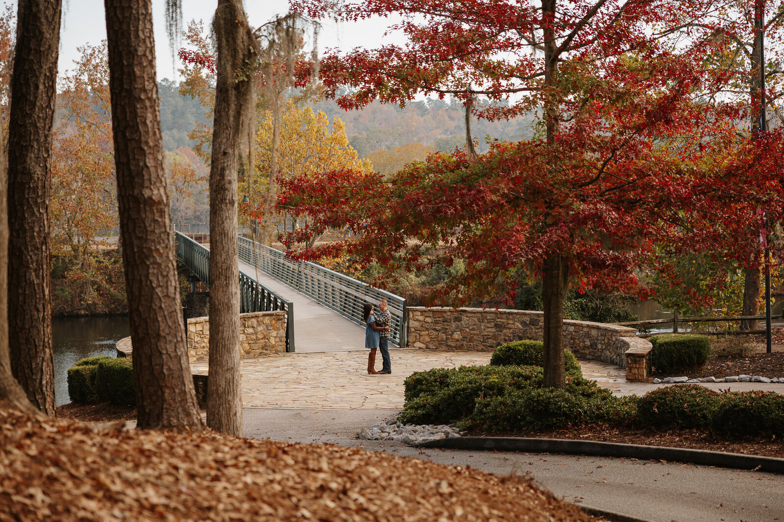 Couples session at Savannah Rapids in Evans GA - couple walking across the stone bridge surrounded by vibrant fall leaves.