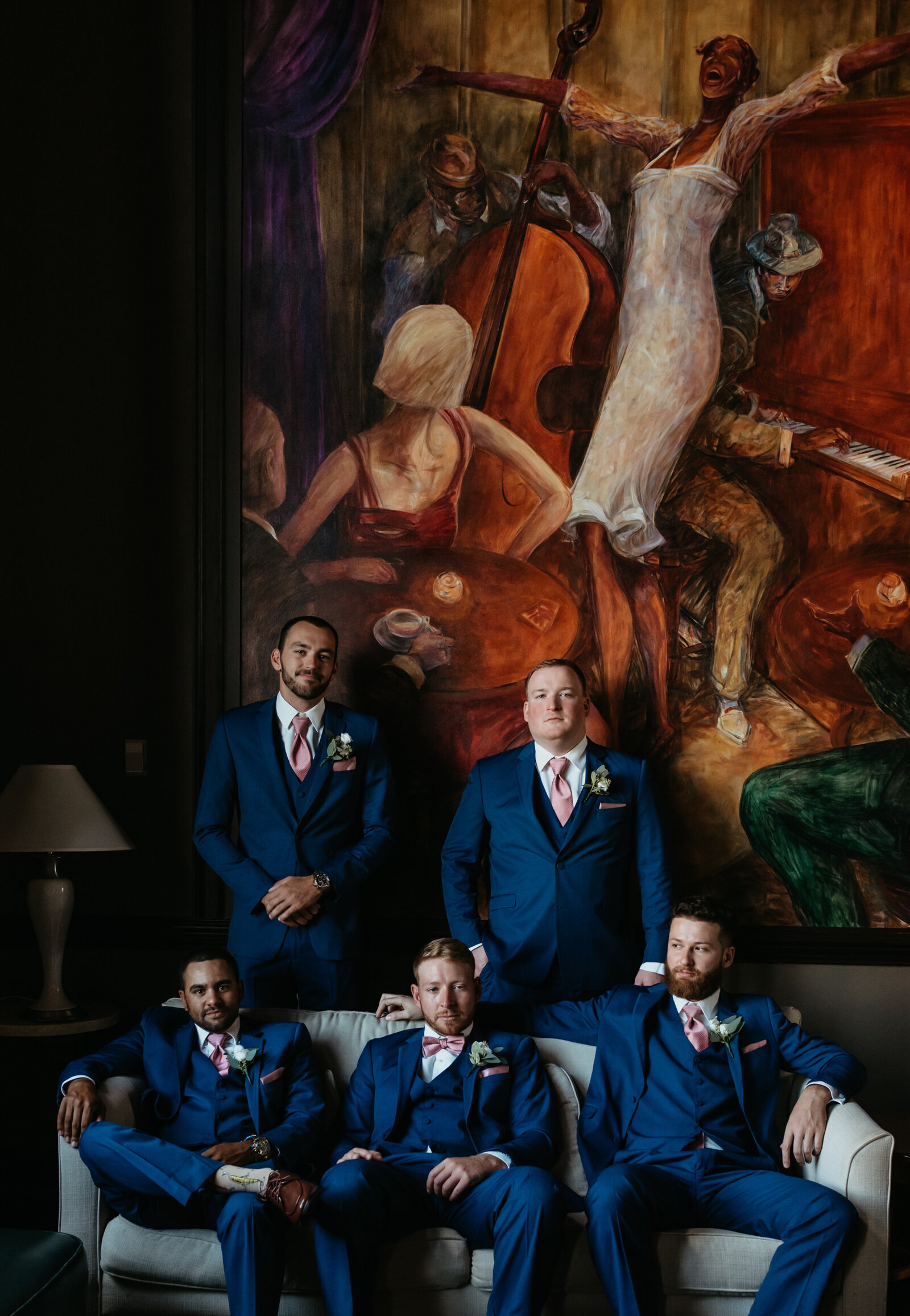 A groom and his groomsmen sit on a couch in front of a large painting