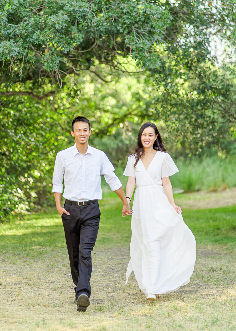 utah engagement photography of an engaged couple walking  through the trees at Highland Glen Park in Lehi