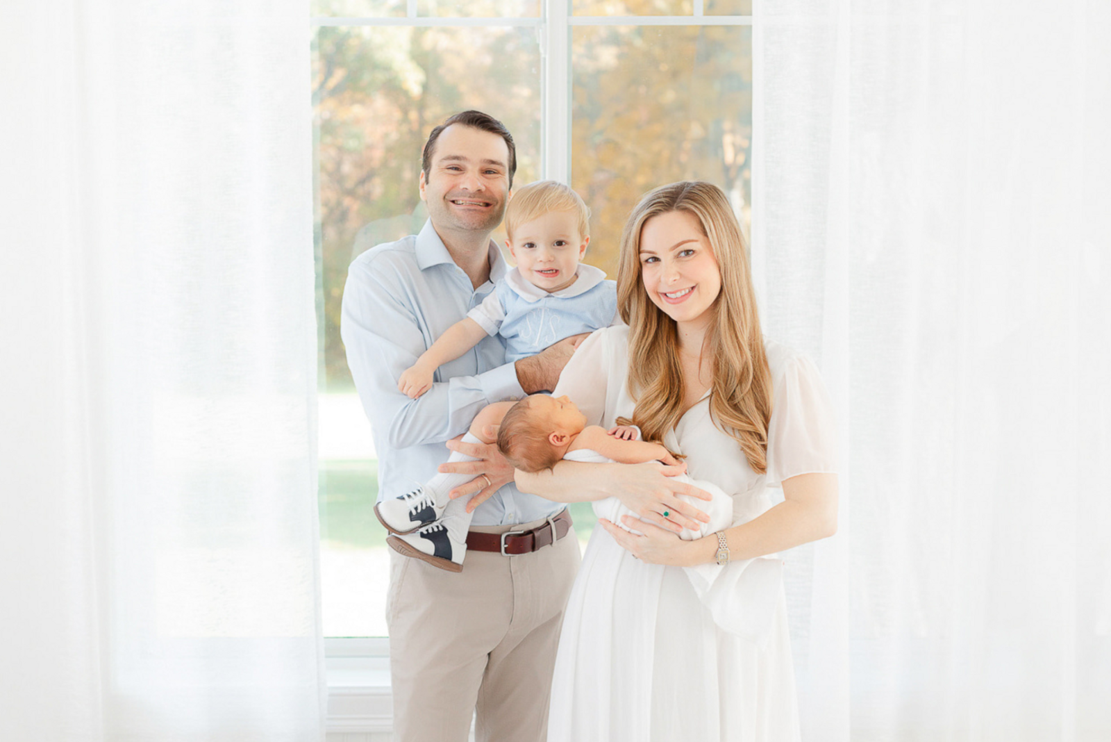 family with toddler and newborn smiles at the camera during boston newborn photoshoot