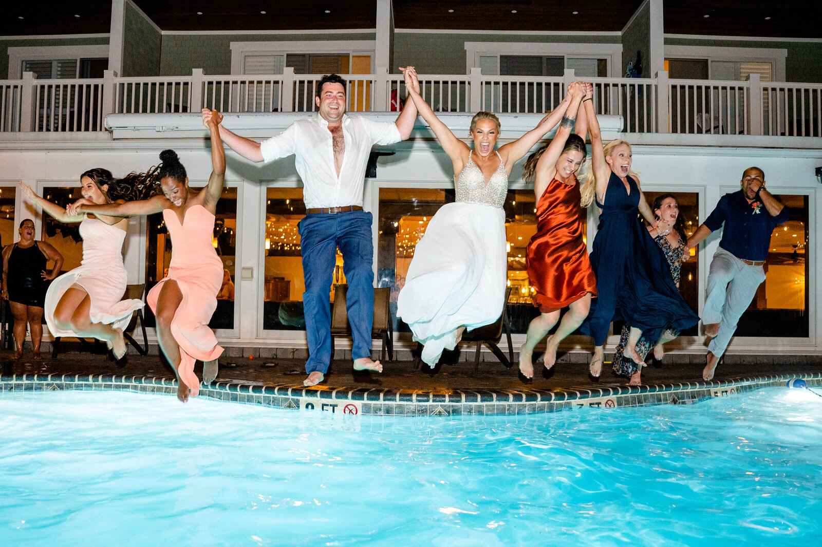 bride, groom and bridal party all holding hands as they jump into the pool at a Jersey shore wedding venue.