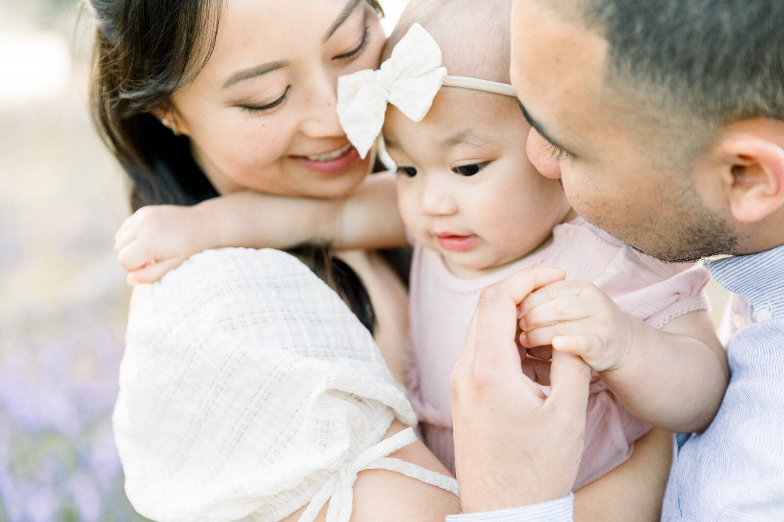 Mom and dad snuggling one year old baby girl in bow taken by Family Photographer Sacramento Kelsey Krall