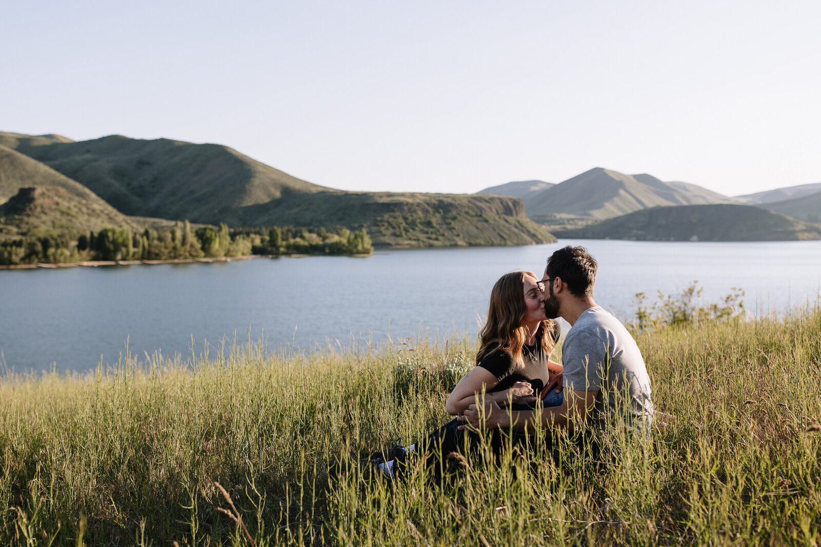 Sweeping lake view behind couple kissing during engagement session at Lucky Peak